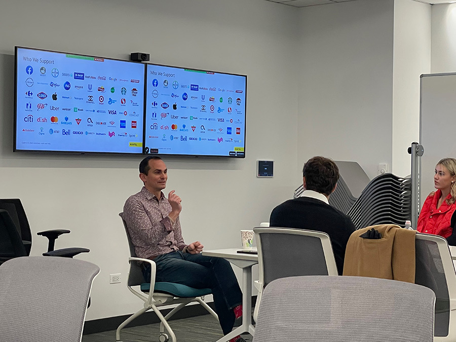 A man in a business suit speaks to a group of people around a conference table.