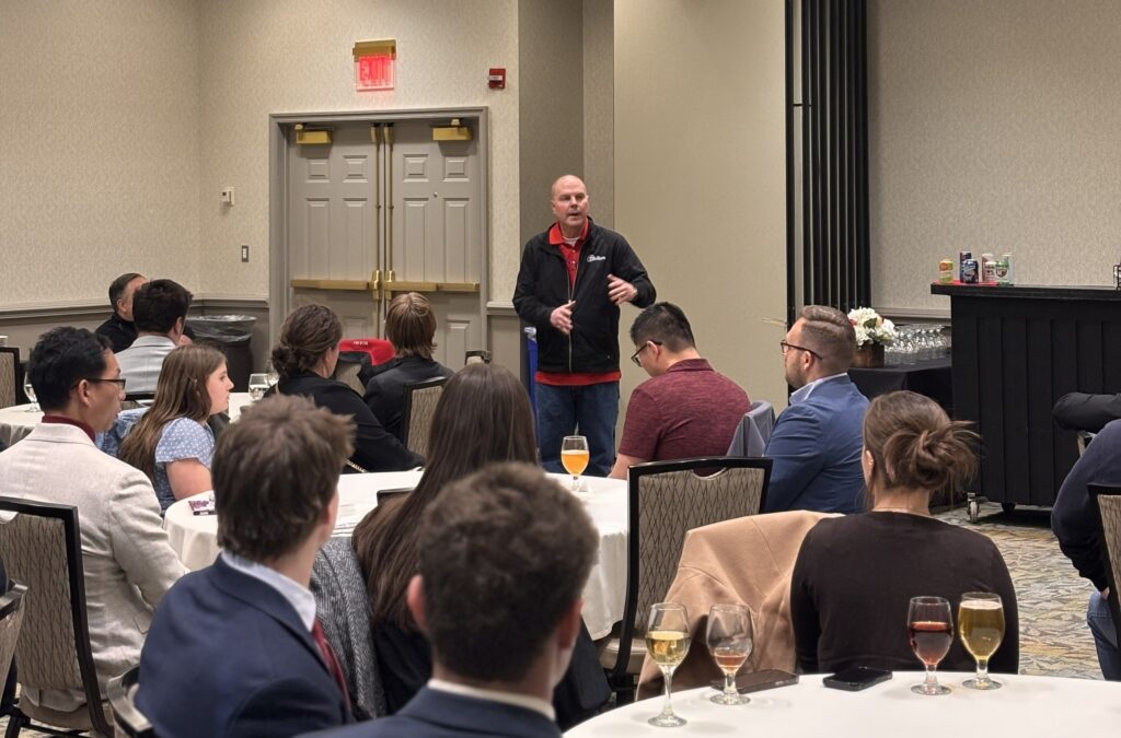 A man speaks at a conference center to guests seated at round tables
