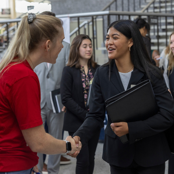 A young professional shaking an interviewer's hand at a career fair.