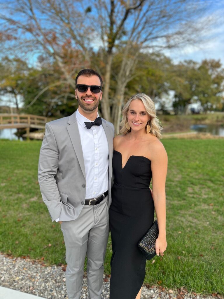 Shannon (Speed) Rex posed with her partner at a park with a bridge, green grass and trees in the background.