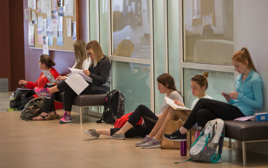 students sitting on the ground and in chairs in a classroom hallway, looking over notes