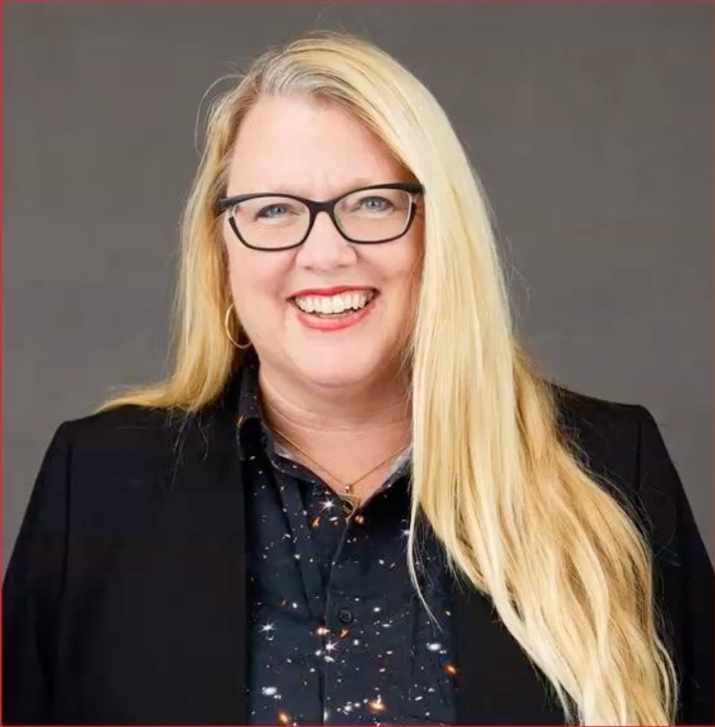 A professional headshot of Barbara Sobhani, a woman with long blonde hair, glasses, and a bright smile. She is wearing a black blazer over a dark shirt patterned with a starry galaxy print, set against a neutral grey background.