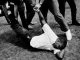 Photo of Non-Violence Resistance Training. A man lies on the ground while a group of men stand over him. Two hold him by his left arm and left leg.