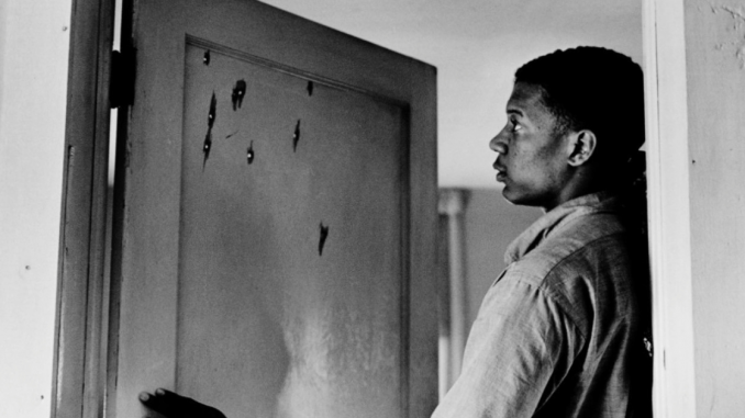 Photo of Jerome Smith looking at bullet holes in Fannie Lou Hamer's door.