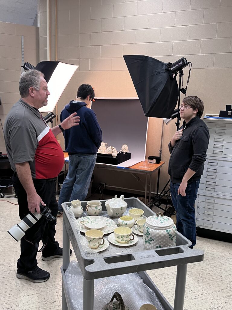 Photographer cart with orcelin dishes, Two male students learning from photographer as he explains his process for photographing museum objects.