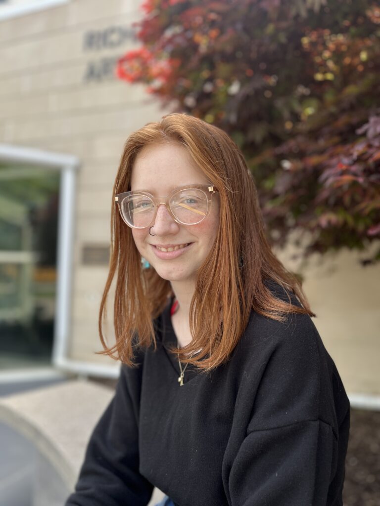 Edgewood High School 2025 graduate Lexi Drake pictured in front of the art museum. Young lady with long red hair with glasses wearing a black sweatshirt.  