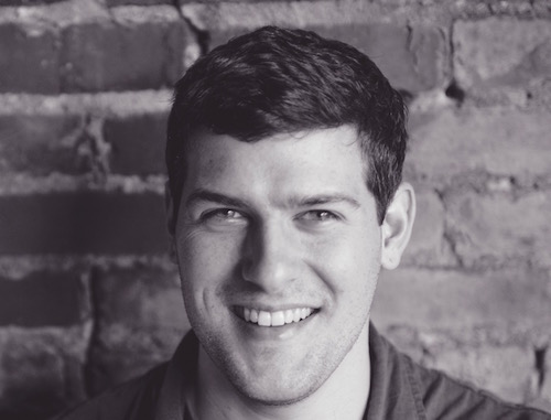 Black-and-white photograph of Miami graduate alum Matt Young smiling broadly, an exposed-brick wall behind him.