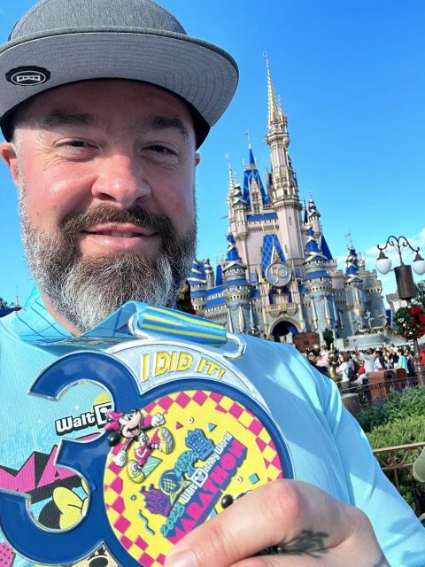 Erich Marinich shows off his completion medal with the Disney castle in the background