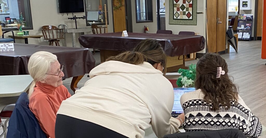 Student leans over a computer with two senior center members.