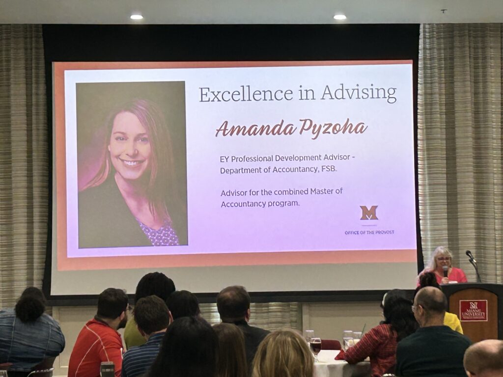 Photo of a gathering showing a slide with Amanda Pyzoha's photo and the words "Excellence in Advising"