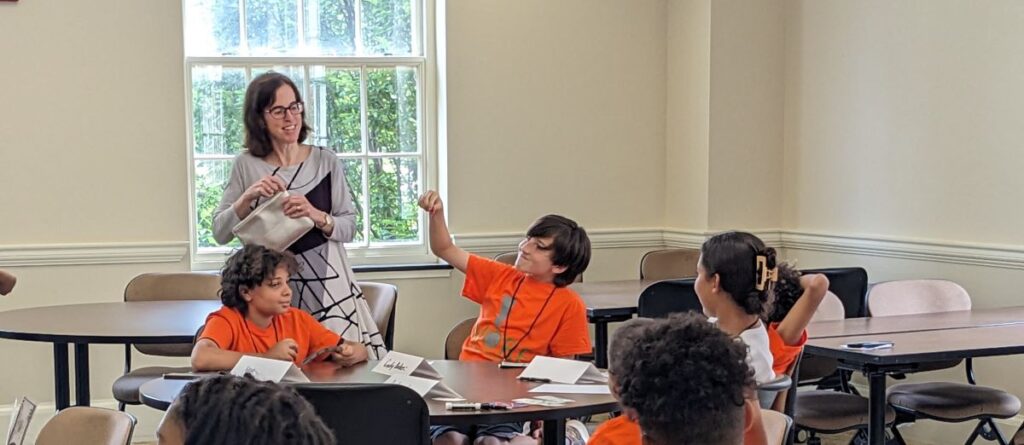 Photo shows Professor Michele Frank with a table of students making an excited gesture