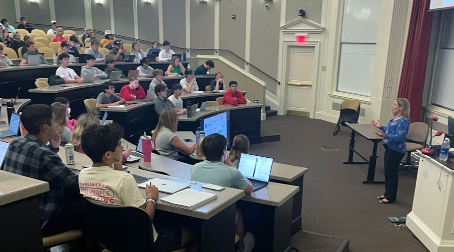 A photo shows Chrissy Walters speaking to a group of students seated at an auditorium