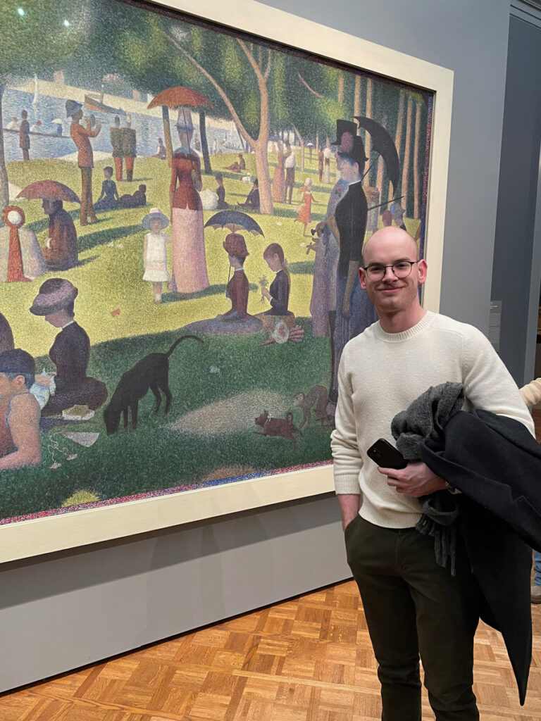 A male student poses in front of a painting.