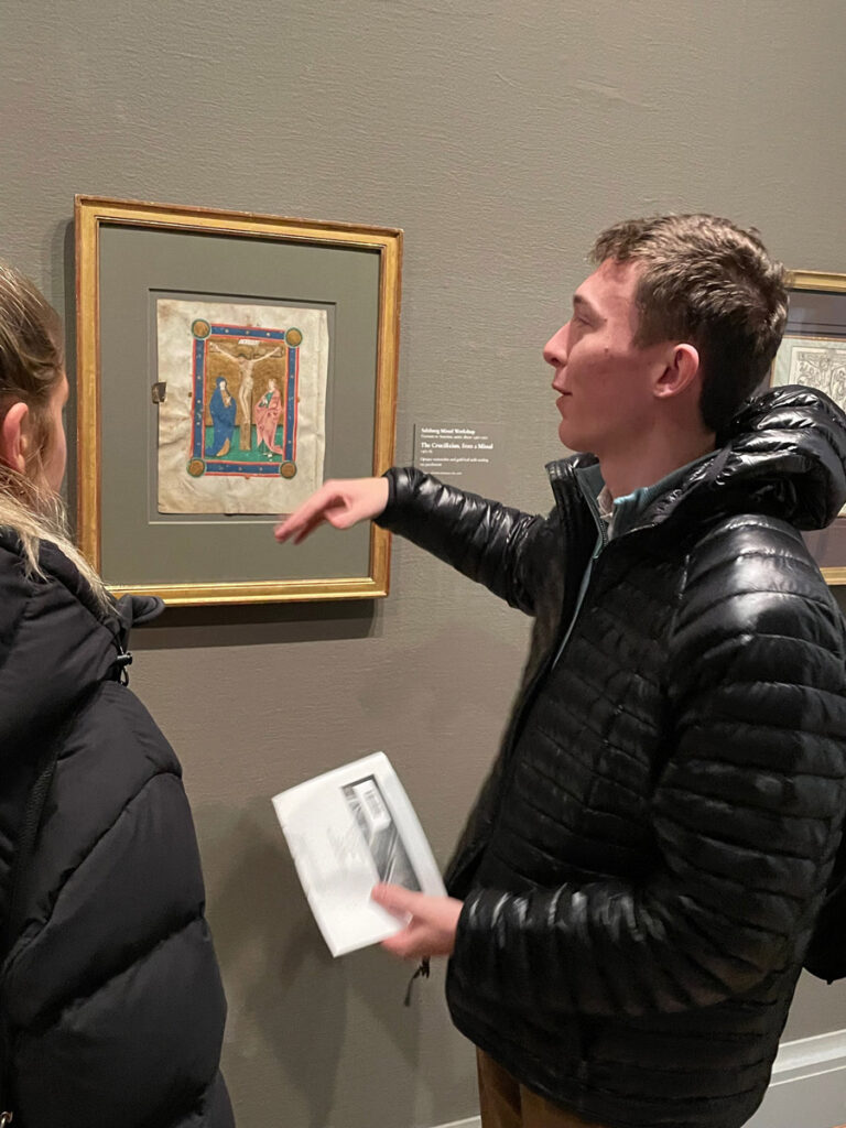 Two students discussing a small painting displayed on a wall