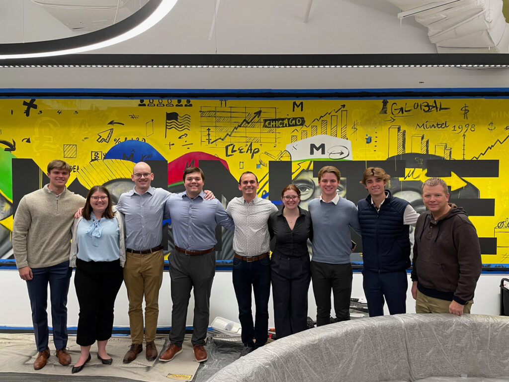 A group of students and professionals pose in front of a brightly colored wall