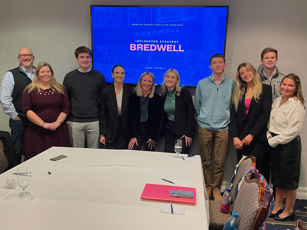 A group of students pose in front of a blue screen showing the title "Bredwell"