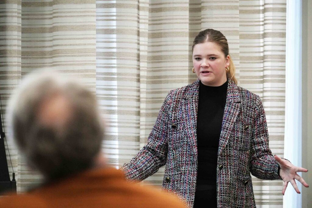 Photo of female student in business attire presenting with the audience blurred in the foreground