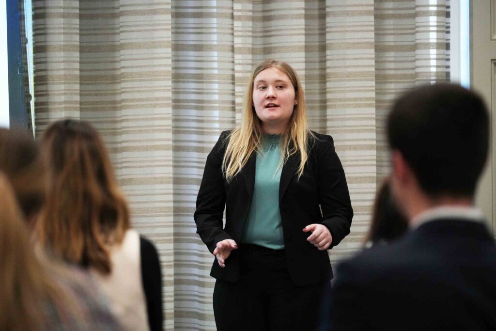 Photo of female student in business attire presenting with the audience blurred in the foreground