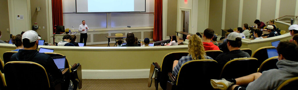 A wide view of a auditorium-style classroom with a speaker in front