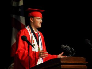 Photo of Jake at the podium in his graduation regalia