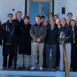 A group of Miami accountancy students with Professor Tim Eaton pose in front of a white brick building