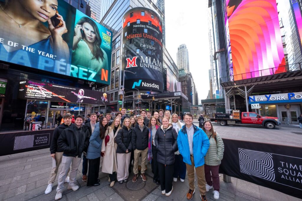 A group of Miami Accountancy students pose with Professor Tim Eaton at Times Square, with Miami University logo displayed above the Nasdaq logo.