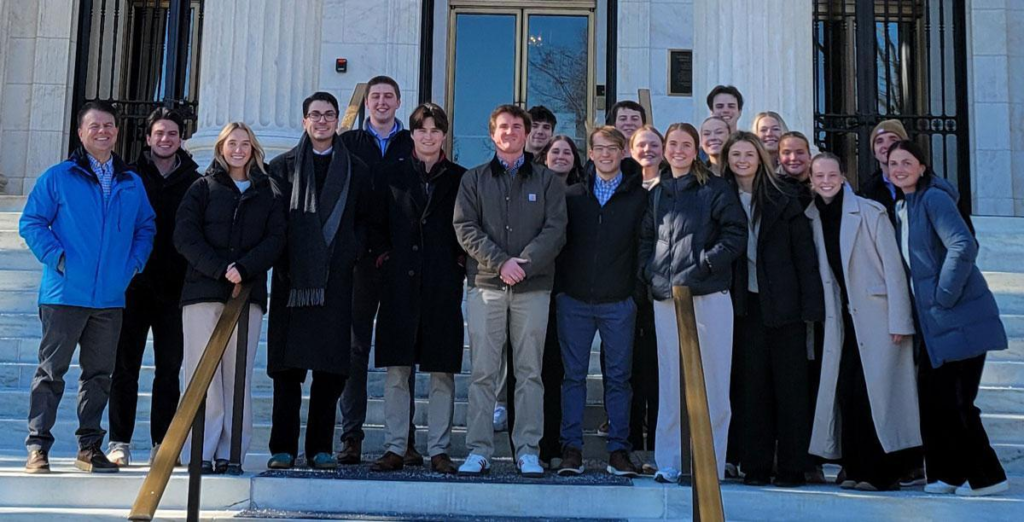 Photo of a group of students standing in front of a white building with large columns