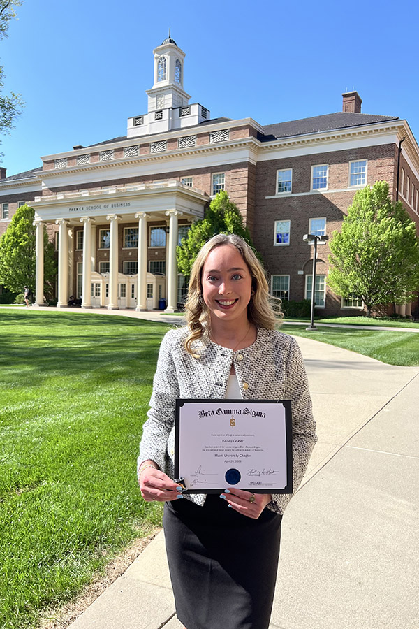 Kelsey posing in front of the Farmer School of Business building while holding a certificate from Beta Gamma Sigma