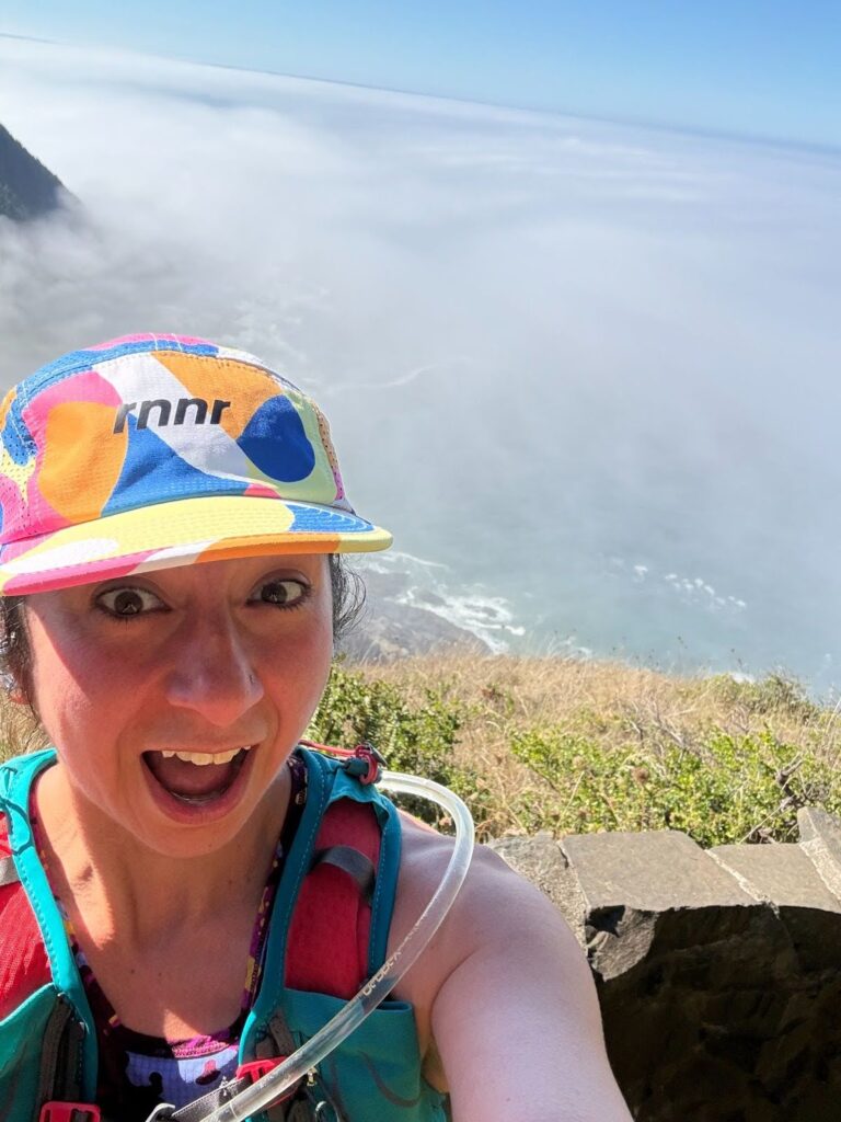 A close-up selfie of Kathayoon Khalil smiling with a scenic, misty, and foggy coastal background at Cape Perpetua, Oregon.