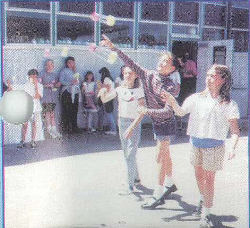 A student in a striped shirt holds a straw-and-hoop glider, preparing to throw it down a hallway where a measuring tape is visible on the floor.