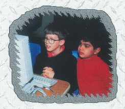 Two young boys in a classroom looking at a 1990s-era computer monitor and keyboard.