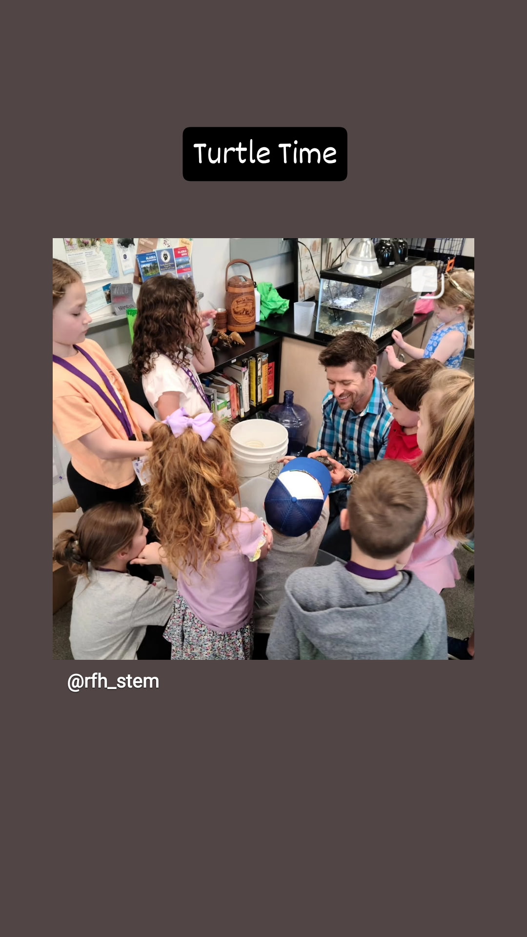 A smiling teacher in a science classroom shows a small turtle to a group of young, curious students gathered tightly around him. A text overlay reads "Turtle Time".