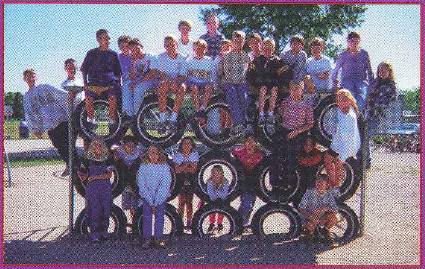 A group of elementary students sitting and smiling inside a grid structure made of stacked black rubber tires.