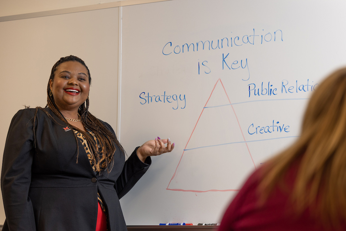 Ashlea Jones, leader of the Academic Marketing team pointing to a whiteboard drawing outlining the importance of strategy, public relations, and creativity as part of communications
