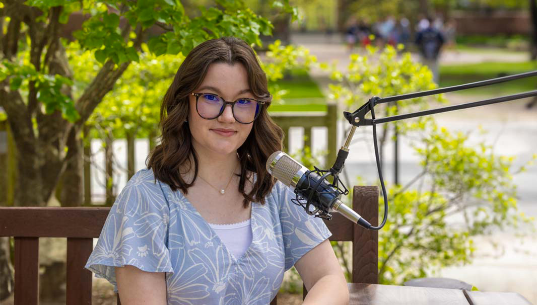 Major Insight podcast host and Miami student Maggie sitting on a park bench outside on a sunny day with a recording microphone