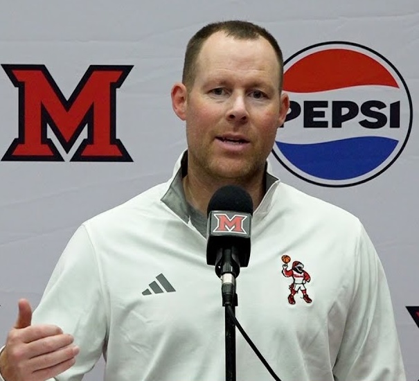 Miami University basketball coach Travis Steele at a post-game press conference wearing a quarter-zip with basketball swoop illustration embroidered.