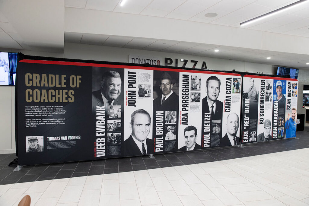 Large banners display the photos and names of Miami football coaches including Weeb Ewbank, John Pont, Ara Parseghian, Carm Cozza, Early Blank, Bo Schembechler, and Sean McVay.