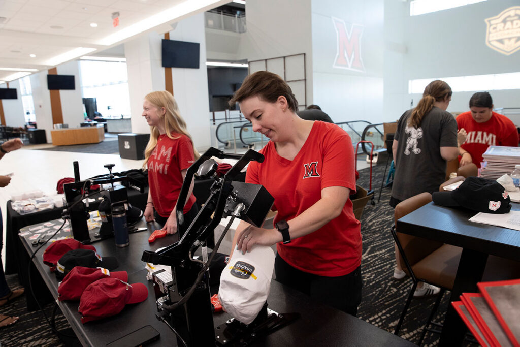 University Communications and Marketing team members apply Miami branded patches to baseball caps.