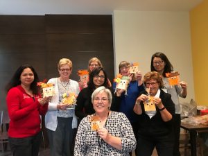 Eight women smiling and holding up a fall-themed paper craft