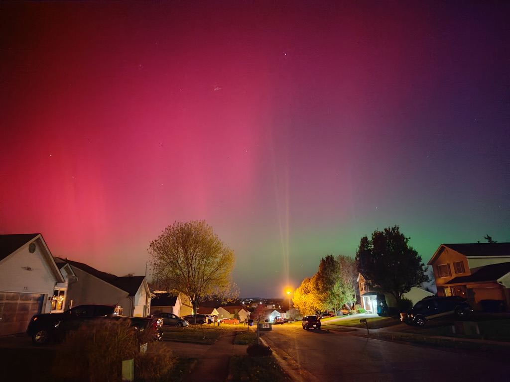 The pink, purple, and green waves of the Northern Lights as seen from a suburban neighborhood