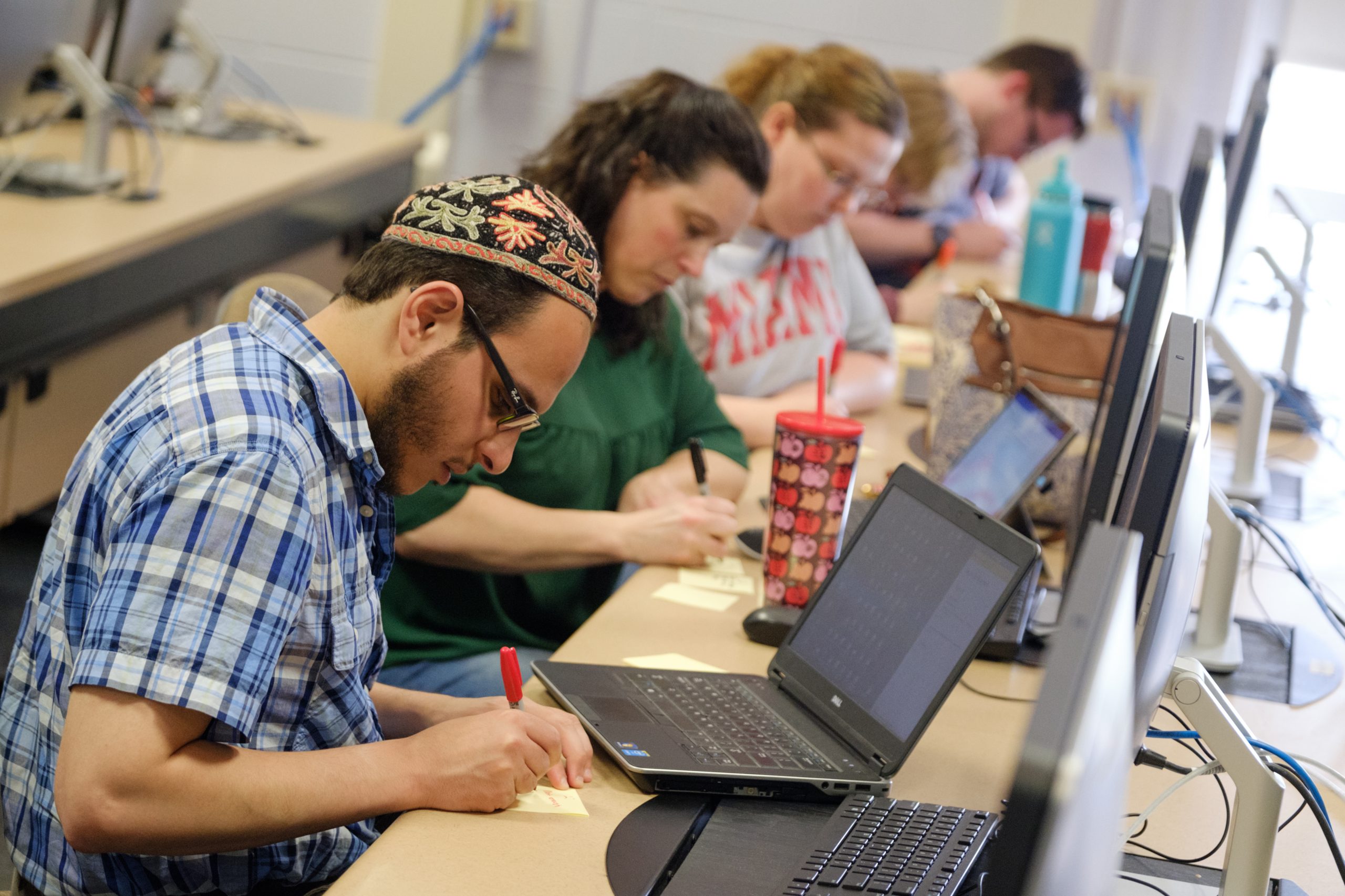 Student takes notes in class with laptop open in front of him.