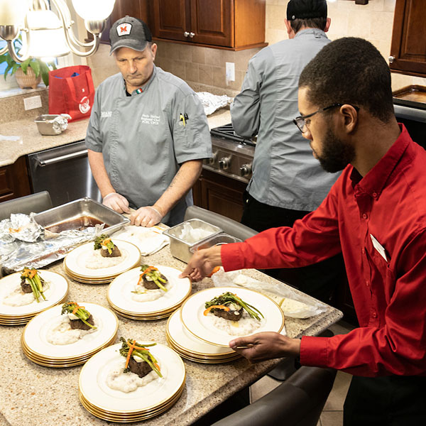 A banquet manager overseeing staff getting ready to serve plates of food