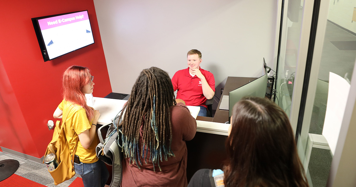 Several students seeking help from a student employee at the Miami University Regionals E-Campus desk