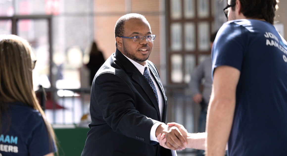 A student shaking hands with a perspective employer at a career fair