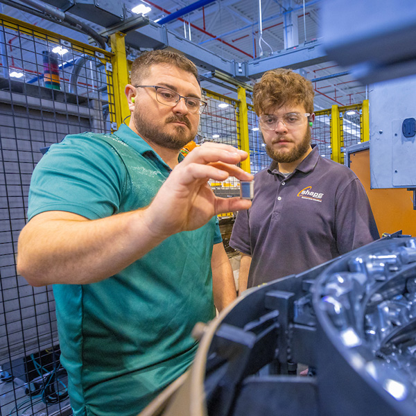 A Work+ student and his supervisor are examining a device in a manufacturing setting at Shape Corporation.