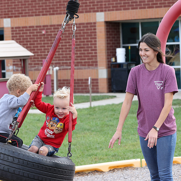 A Work+ student pushing preschoolers on a tire swing at a local YMCA.