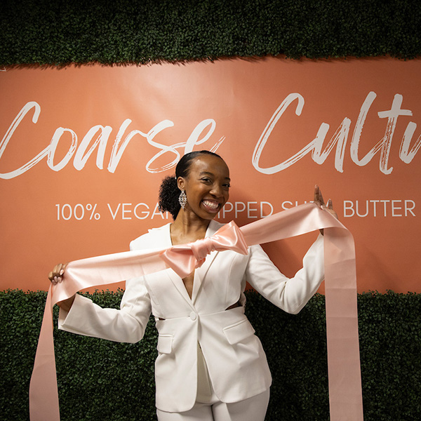 VaLanDria Smith-Lash, 2023 alumnae, standing in front of her branding for her "Coarse Culture" products.