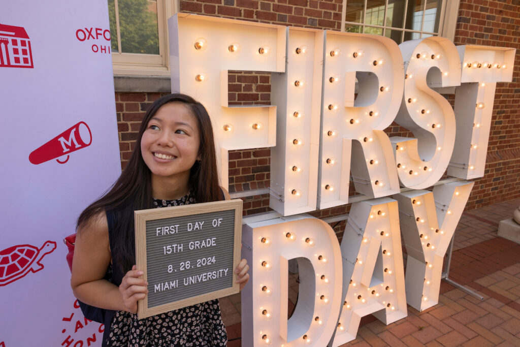 A young woman standing in front of "First Day" light-up sign letters at Miami University