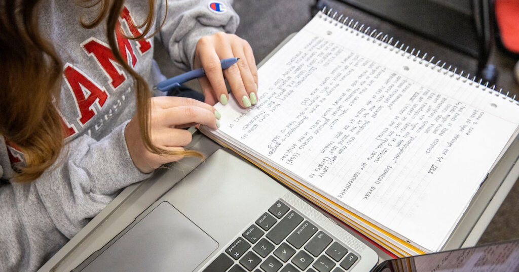 A college student reviewing her hand-written notes next to her computer.