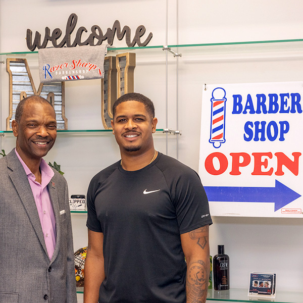 A small business barber shop owner standing next to one of his investors